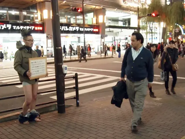 “Put shoses on the head”. Instructions posted on the board, performer, passersby. 2012. Instructions: “Please exchange your shoes”, “Please exchange your pants”, “Please exchange your shirt”