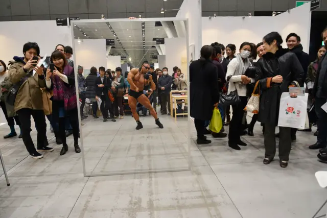 “Photographer: Bodybuilder”. Bodybuilder, single-lens reflex camera, mirror, assistant, exhibition space. 2012/2014. Art Fair Tokyo 2014
